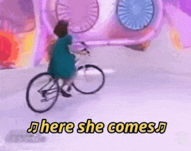 a woman is riding a bicycle with the words here she comes in the background