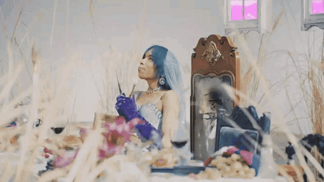 a woman with blue hair is sitting in front of a mirror with a demon coming out of it .