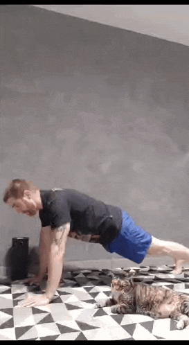 a man is doing push ups on a checkered floor with a cat laying on the floor .