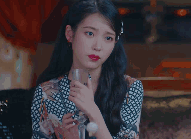 a woman covering her mouth with her hand while holding a glass