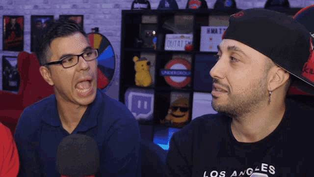 a man wearing glasses and a los angeles shirt talks into a microphone