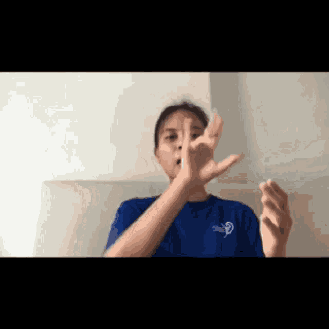 a woman in a blue shirt is making a funny face with her hands .