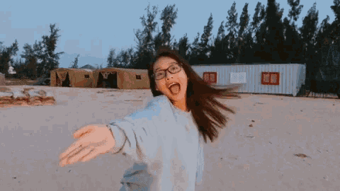 a girl with glasses is standing on the beach with her arms outstretched