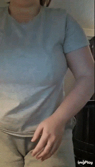a woman in a blue t-shirt and grey pants is standing in a kitchen .