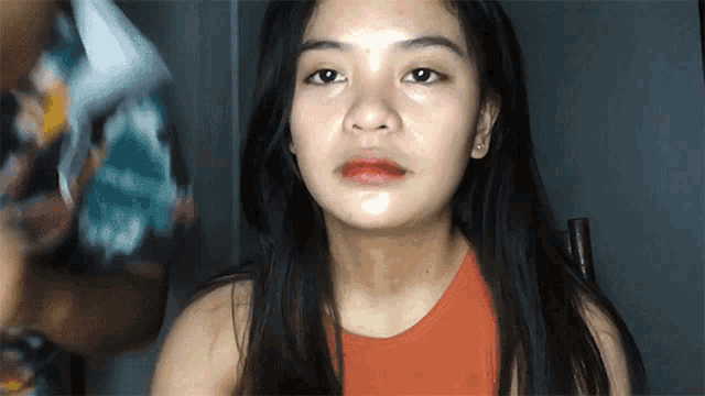 a young woman with long black hair is wearing a red tank top