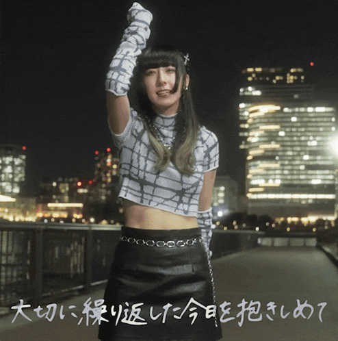 a woman in a crop top and a black skirt is standing in front of a city at night