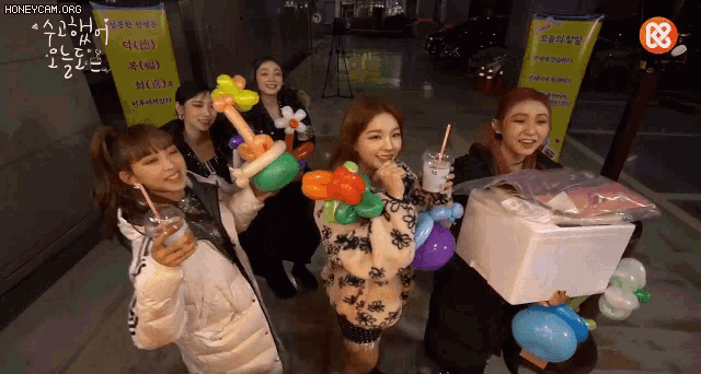 a group of girls holding balloons and drinks in front of a sign that says honeycam org
