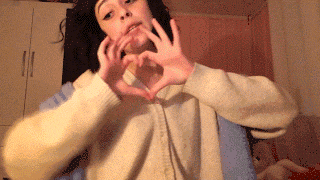a girl in a white sweater making a heart with her hands