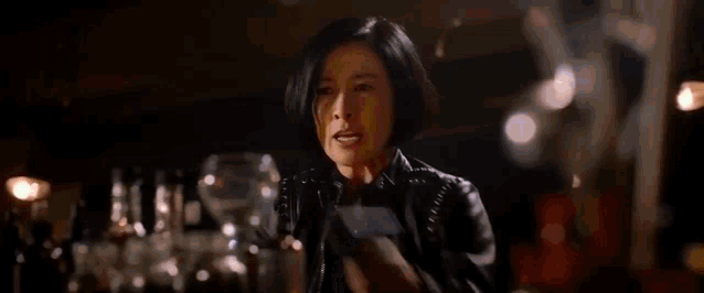 a woman in a leather jacket is holding a gun in her hand and shooting it .