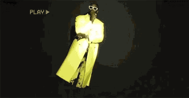 a man in a yellow coat and sunglasses is holding a gun in his hands .