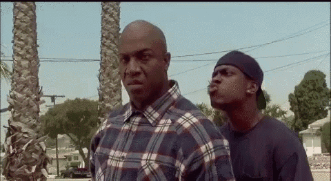 two men are standing next to each other on the side of the road . one of the men is wearing a plaid shirt .