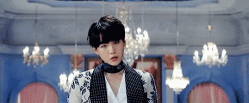 a young man wearing a choker and a jacket is standing in a room with a lot of chandeliers .