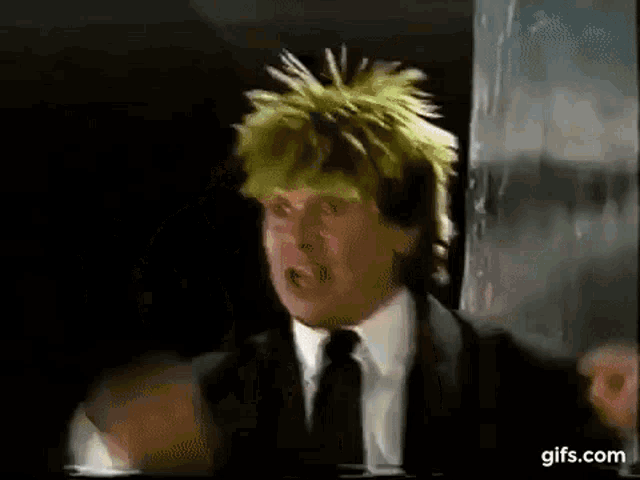 a man in a suit and tie with a yellow wig is making a funny face .