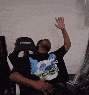 a man sitting in a gtracing chair with his hand up in the air