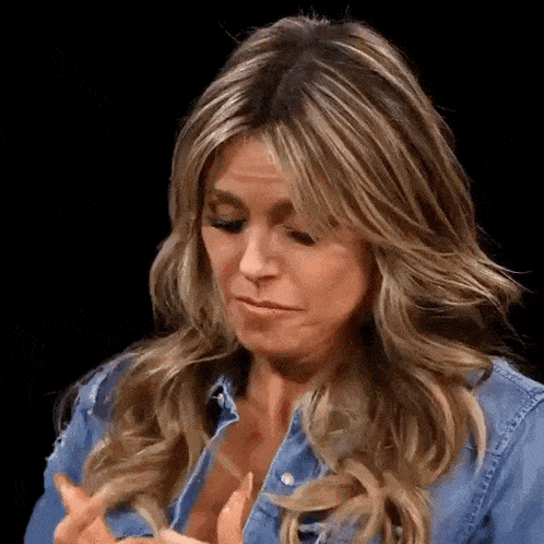 a woman with long blonde hair is wearing a denim shirt and holding a doll .