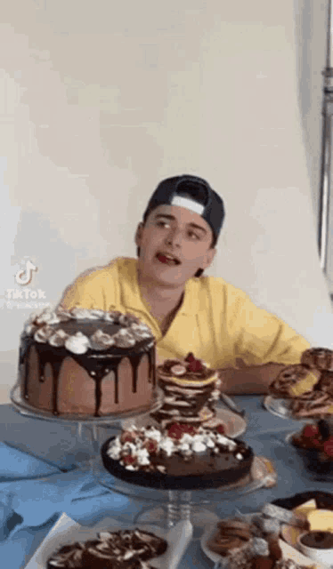 a man in a yellow shirt is sitting at a table with a lot of cakes on it .