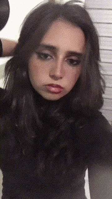 a woman with long dark hair is wearing a black turtleneck sweater and holding her hair dryer .