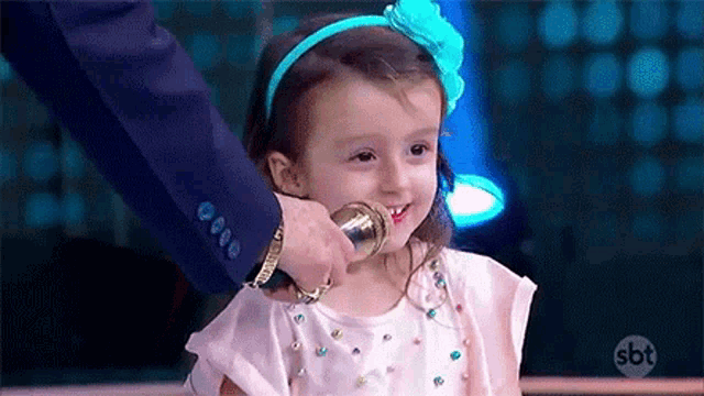 a little girl is smiling while holding a microphone in front of her face .