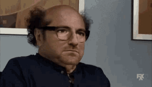 a bald man with glasses and curly hair is making a funny face .