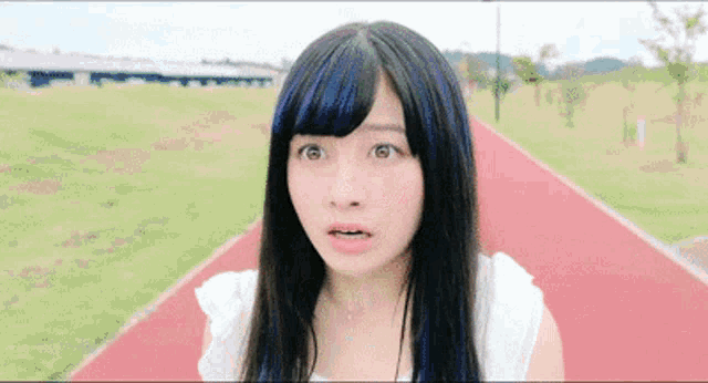 a young woman with long black hair and blue streaks is standing on a red track .