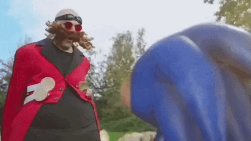 a man in a red jacket and goggles is standing next to a blue sonic .