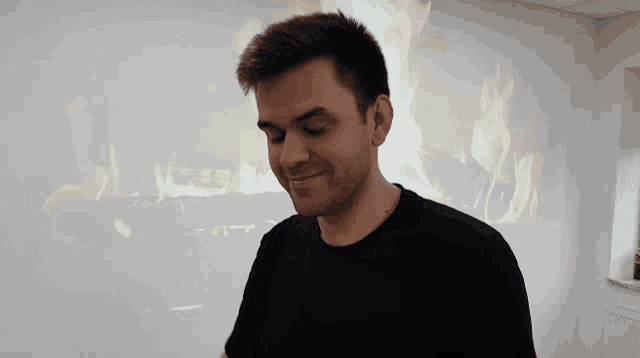 a man in a black shirt is smiling in front of a fire behind him