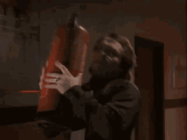 a man in a hooded jacket is holding a red fire extinguisher .