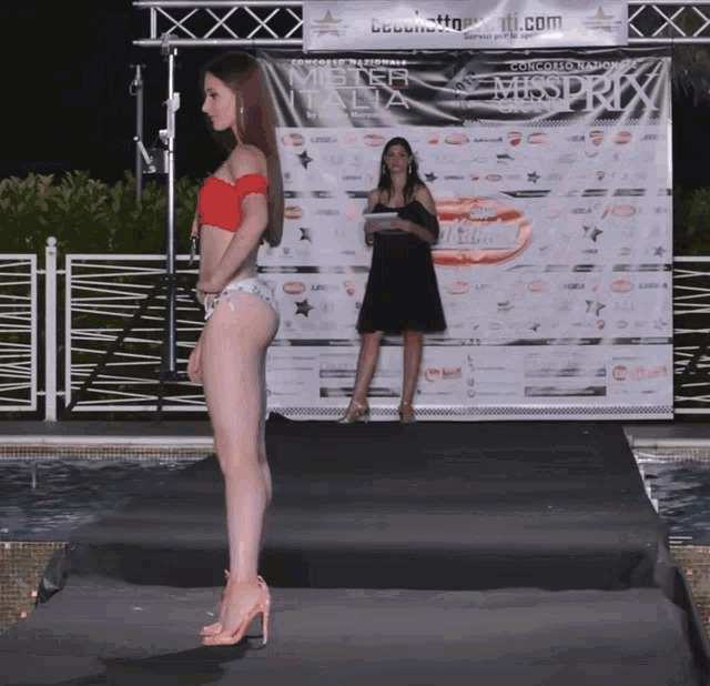 a woman in a bikini walks down a runway in front of a mister italia sign