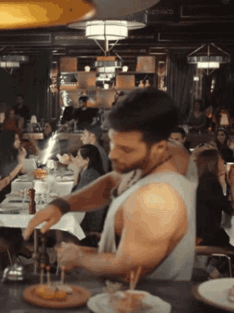 a man in a tank top is standing in front of a crowd of people in a restaurant