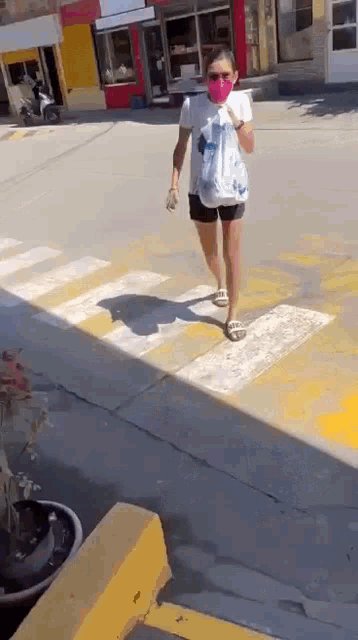 a woman wearing a mask is crossing a street .
