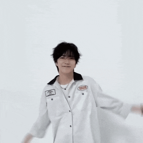 a young man wearing a white shirt and blue jeans makes a heart shape with his hands