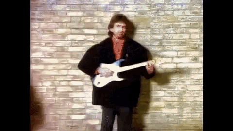 a man is standing in front of a brick wall playing a guitar .