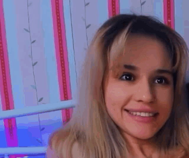 a close up of a woman 's face with a pink and blue striped wall behind her .