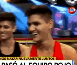 a man in a red tank top is smiling while standing next to another man in a black tank top