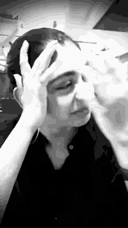 a woman in a black shirt is holding her head with her hands .