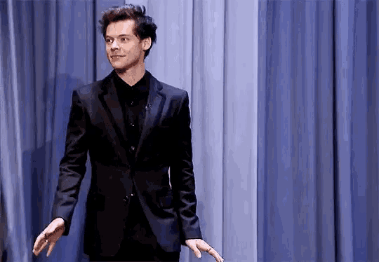 a man in a suit and black shirt is standing on a stage with his hands outstretched .