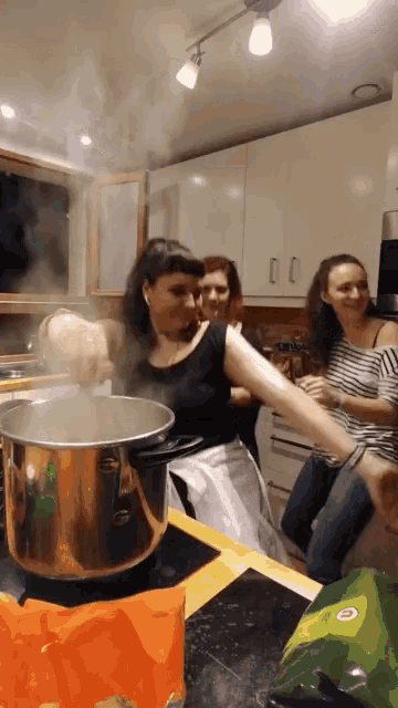 a woman stirs a pot of boiling water in a kitchen with other women