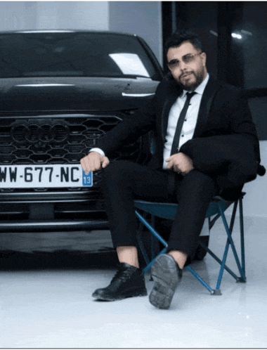 a man in a suit sits in front of an audi with a license plate that says ww-677-nc 13