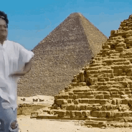 a man in a white shirt is standing in front of a large pyramid .