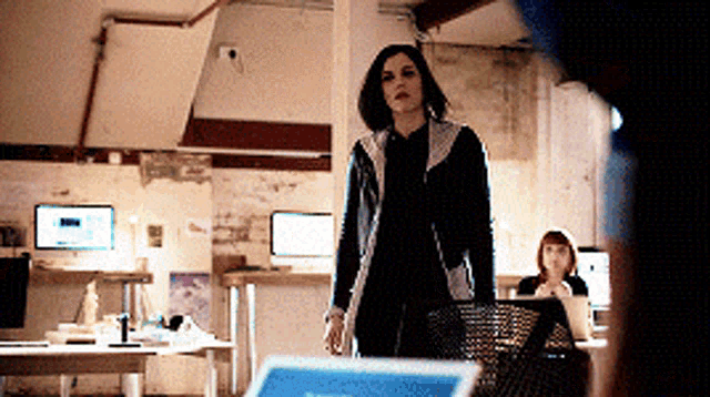 a woman in a black jacket is standing in front of a laptop computer