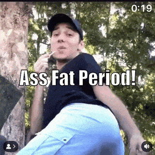 a man is standing next to a tree with a cigarette in his mouth and says `` ass fat period '' .