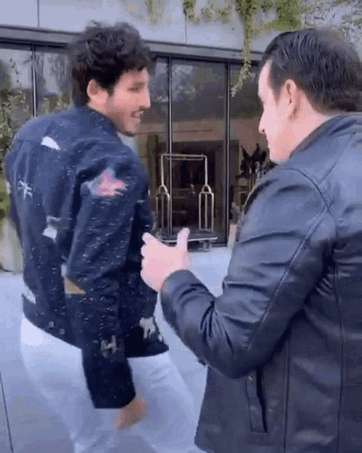 two men are standing next to each other in front of a building .