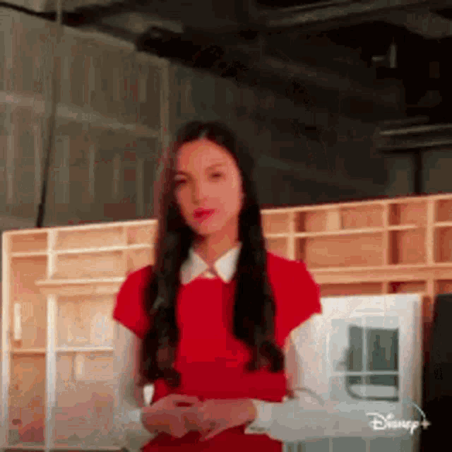a woman in a red dress and white shirt is standing in front of a wooden wall in a room .