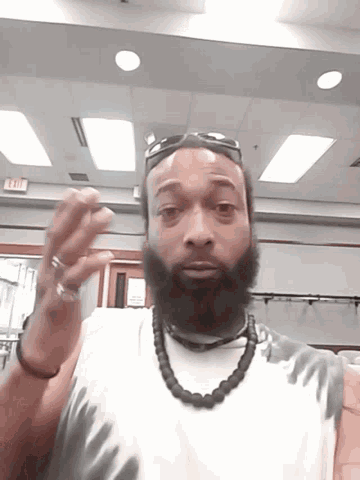 a man with a beard is standing in a room with an exit sign on the wall behind him