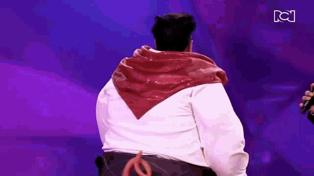 a man with a red scarf around his neck is standing in front of a purple background