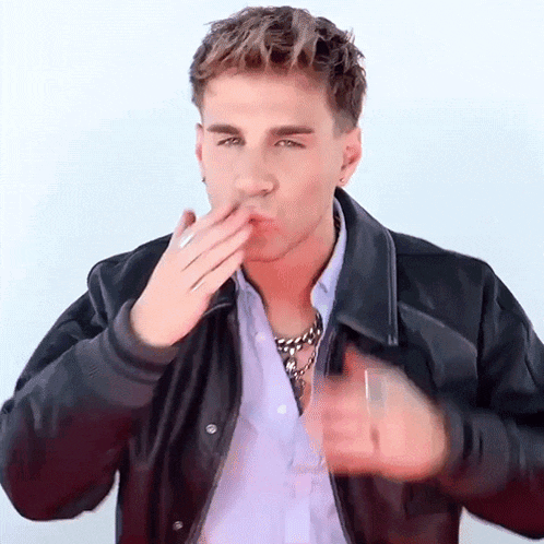 a young man wearing a leather jacket and a necklace is blowing a kiss .