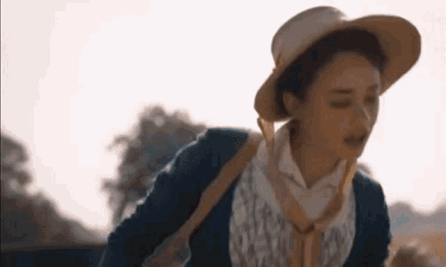 a woman wearing a hat and a blue sweater is walking in a field .