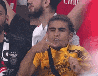 a man in a yellow shirt is making a funny face while sitting in a stadium .
