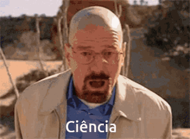 a bald man with glasses and a beard is wearing a tan jacket and a blue shirt .