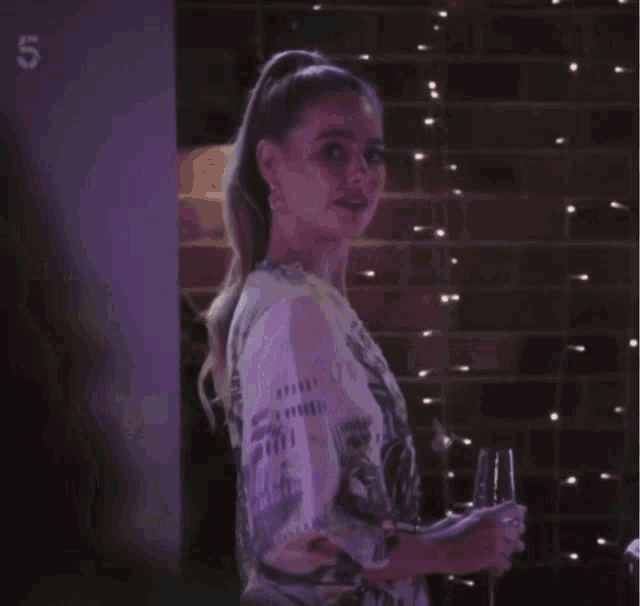 a woman stands in front of a wall with purple lights and the number 5